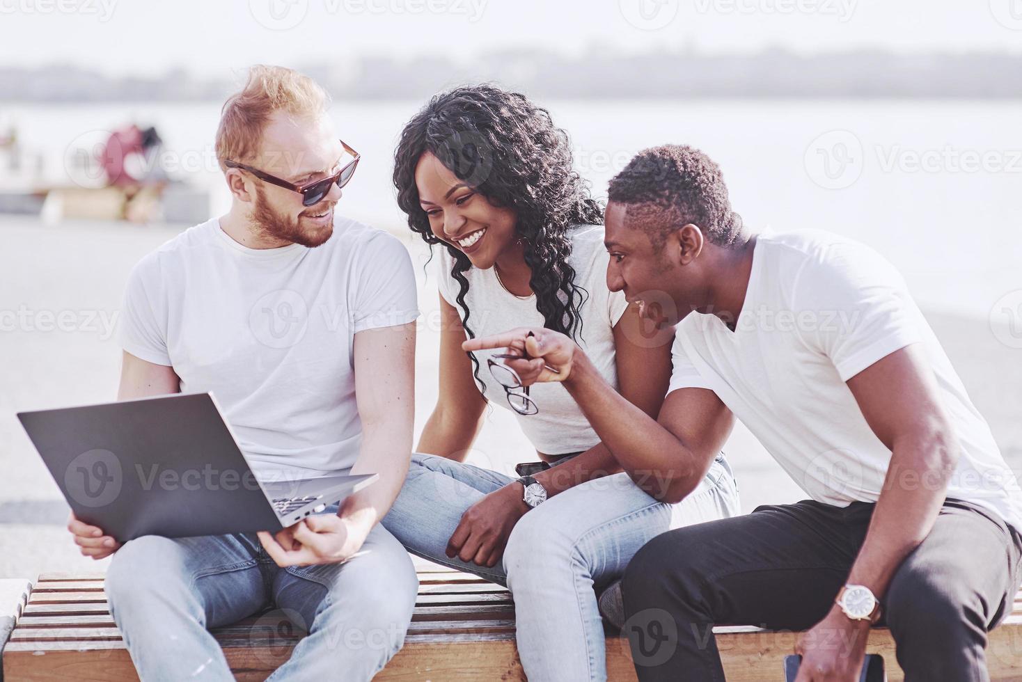 lindos amigos multi-étnicos usando um laptop na rua. conceito de estilo de vida jovem foto