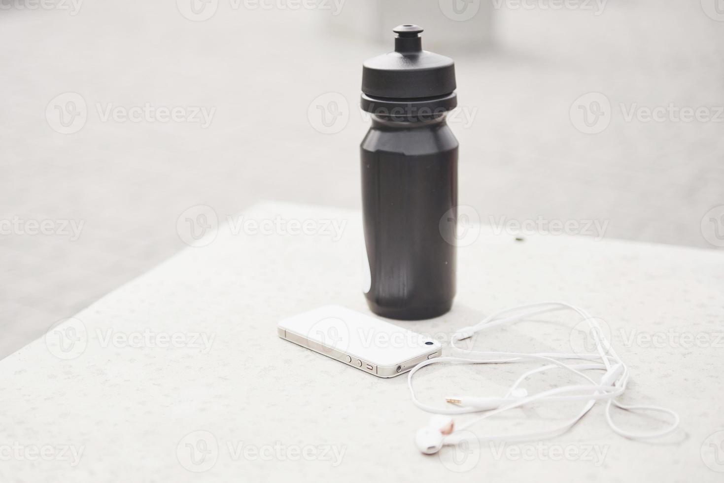 fones de ouvido do telefone e uma garrafa de água ao ar livre. acessórios para esportes de corrida foto