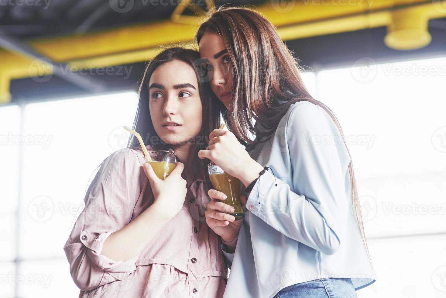 duas lindas gêmeas passam o tempo bebendo suco. irmãs relaxando em um café e se divertindo juntas e sussurrando foto