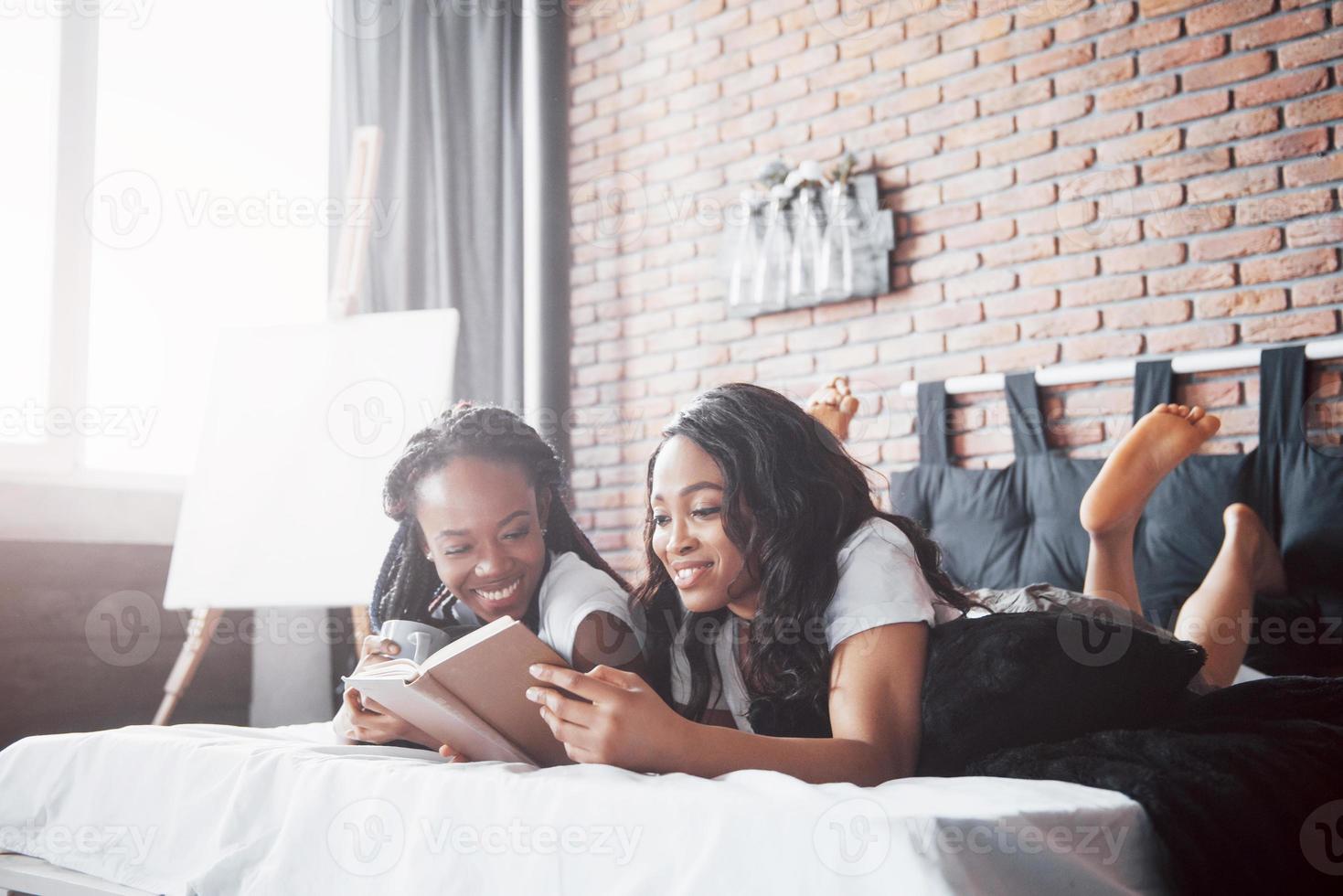 duas linda garota africana em pijamas sorrindo, sentado na cama em casa, acordaram de manhã em um dia ensolarado. foto