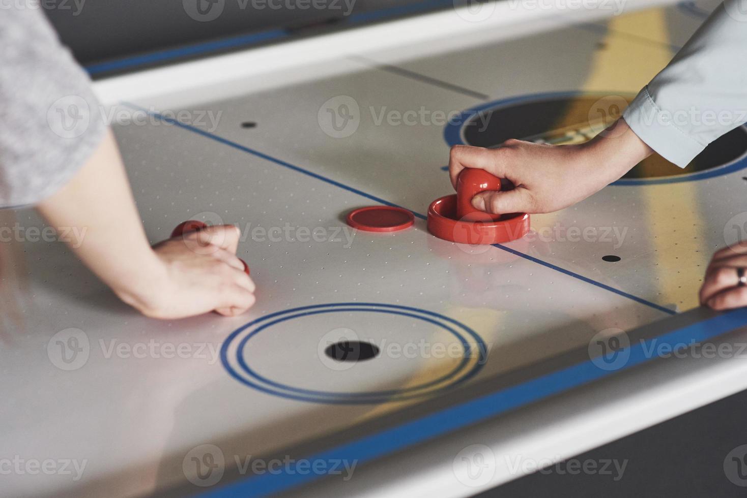 mãos de jovens segurando o atacante na mesa de air hockey na sala de jogos foto