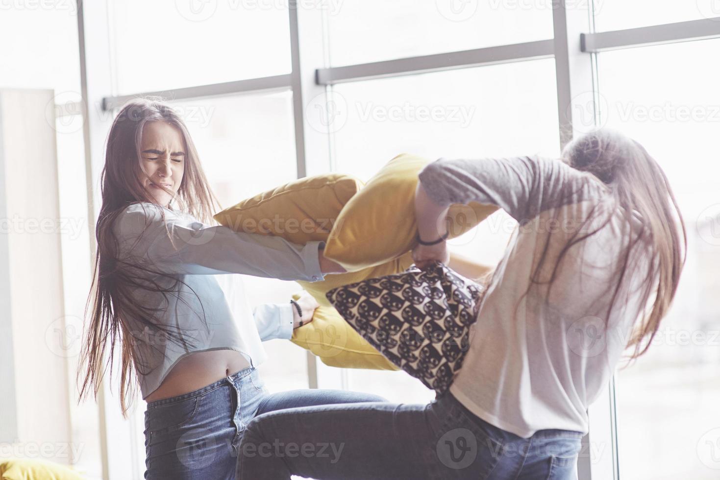 duas lindas irmãs gêmeas passando um tempo juntas lutando com travesseiros. irmãos se divertindo em casa conceito foto