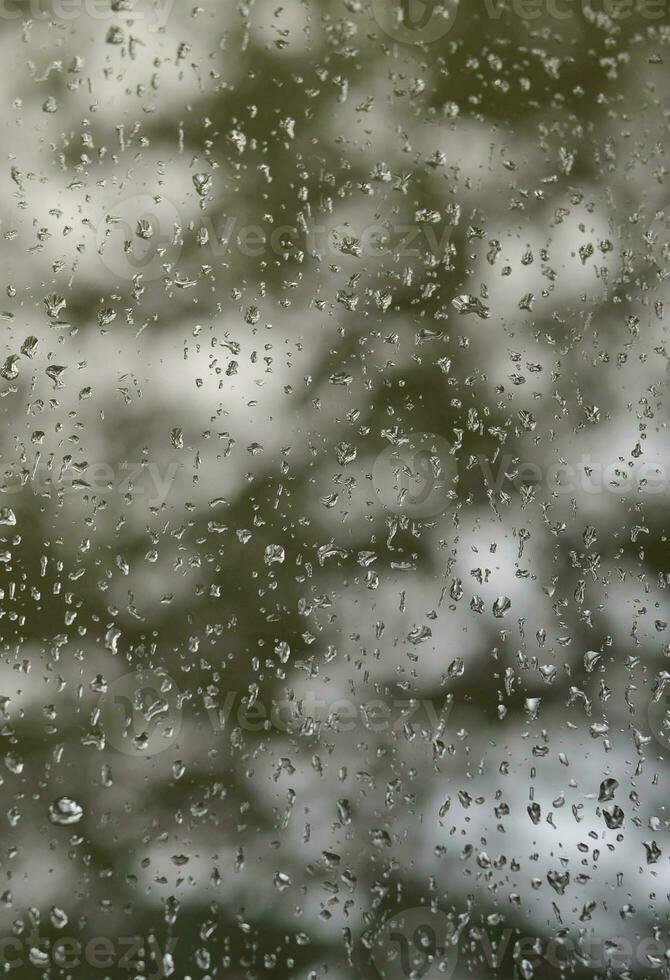 uma foto de chuva cai no vidro da janela com uma visão turva das árvores verdes florescendo. imagem abstrata mostrando condições de tempo nublado e chuvoso