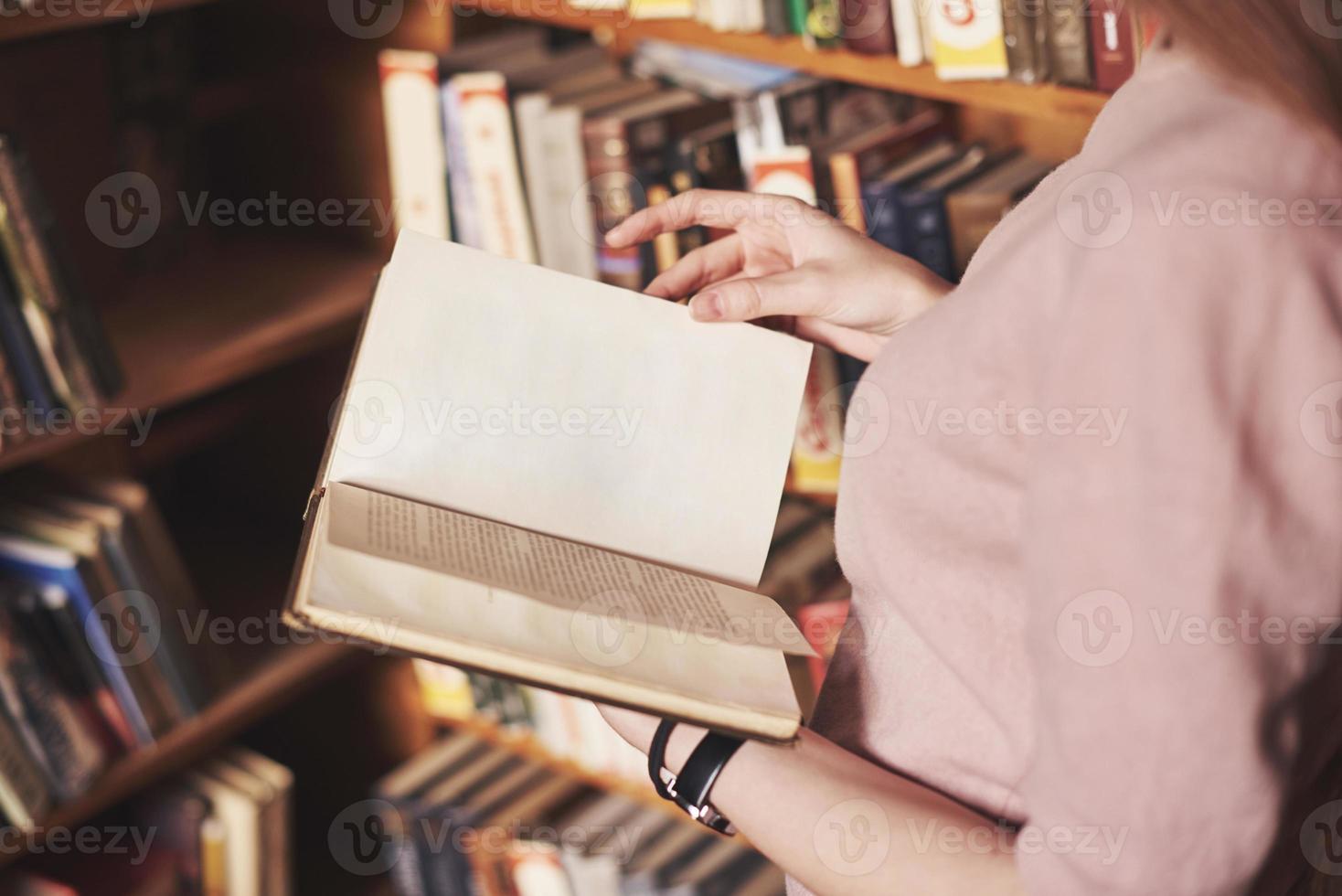 jovem e atraente estudante bibliotecária lendo um livro entre as estantes da biblioteca foto