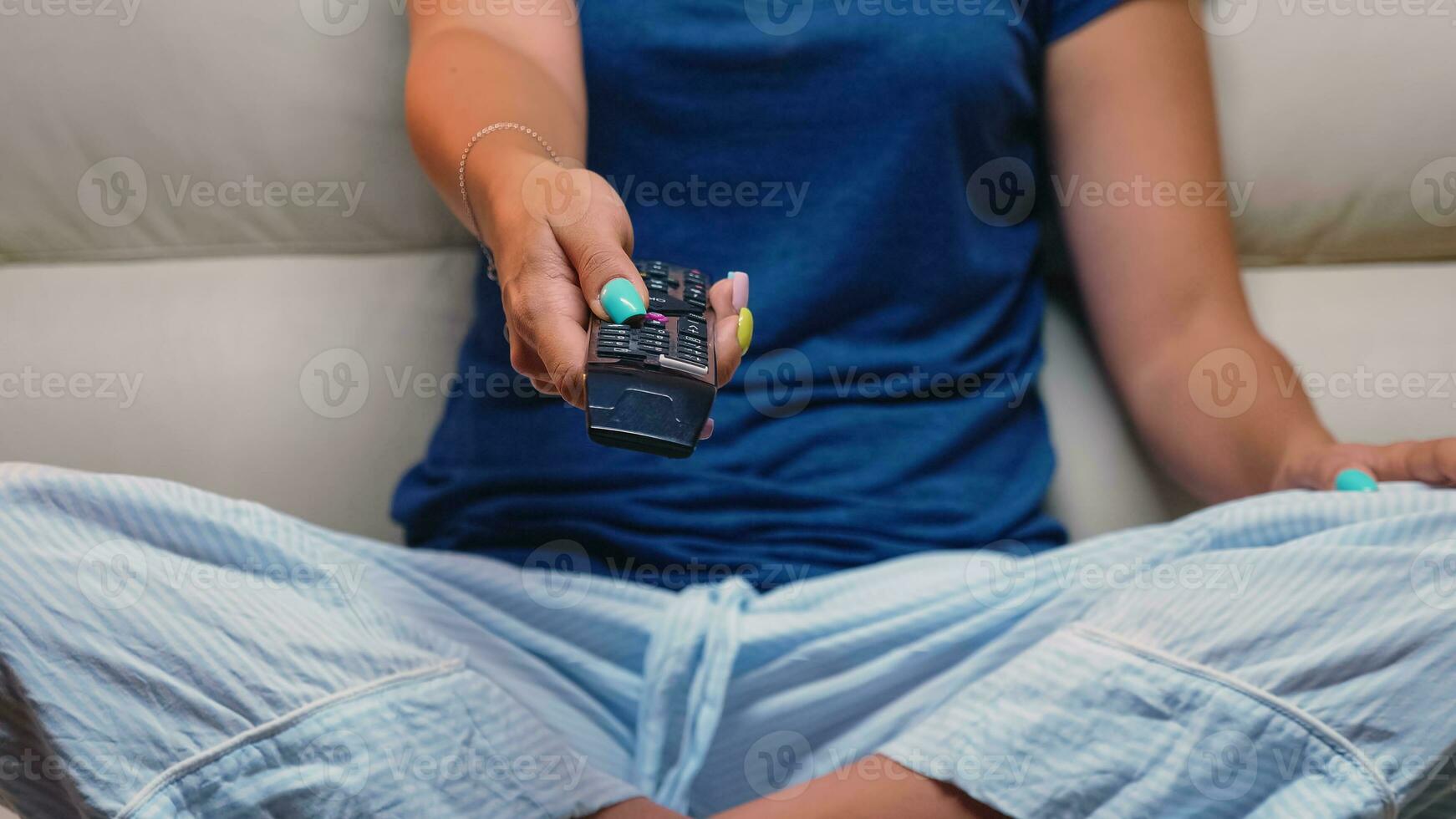 fechar acima tiro do controlador dentro mulher mão enquanto sentado em sofá. controlo remoto ao controle dentro a mãos do pessoa apontando para televisão, pressionando a botão e mudando canais sentado dentro frente do televisão. foto