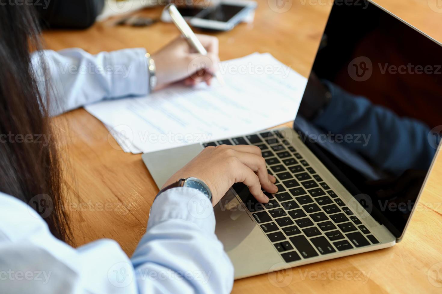 as funcionárias do escritório estão fazendo anotações e usando o laptop. foto