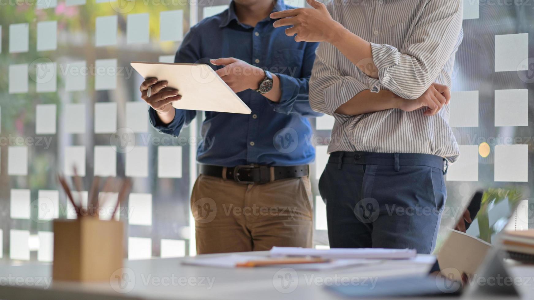 dois homens asiáticos usando um tablet. eles se levantam para consultar o trabalho para apresentar aos clientes no escritório contemporâneo. foto