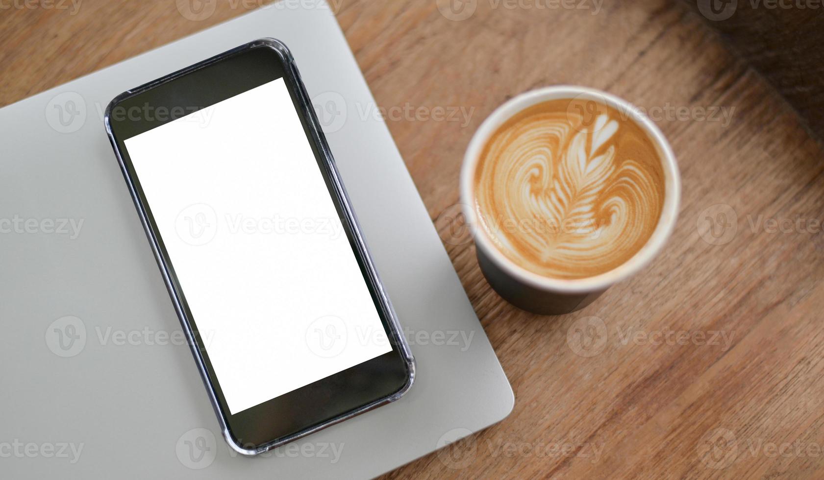 close-up do smartphone de tela em branco de maquete no laptop e textura de coração com café com leite no piso de madeira, vista superior um tiro. foto