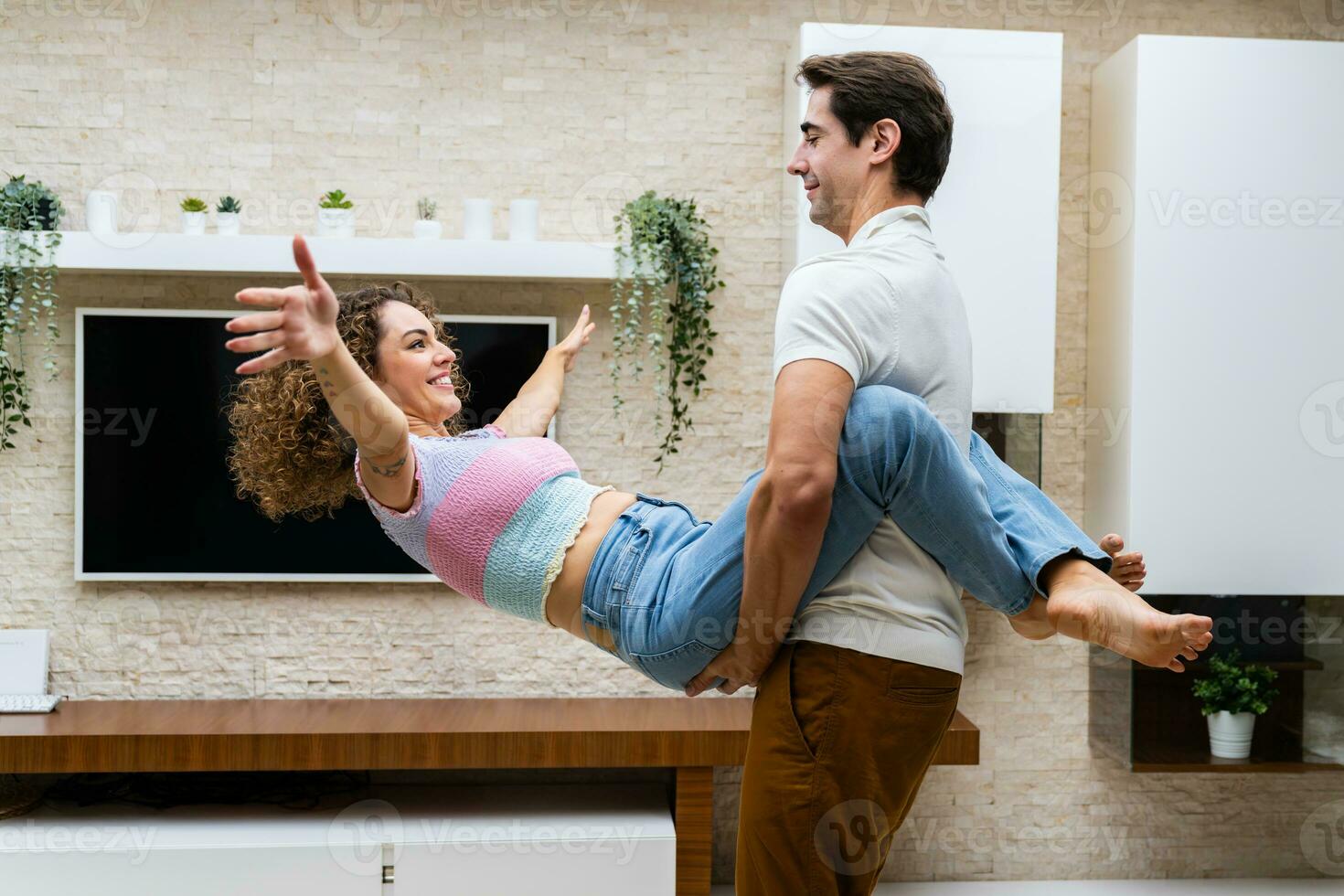 alegre casal abraçando contra televisão e em vaso plantas às casa foto