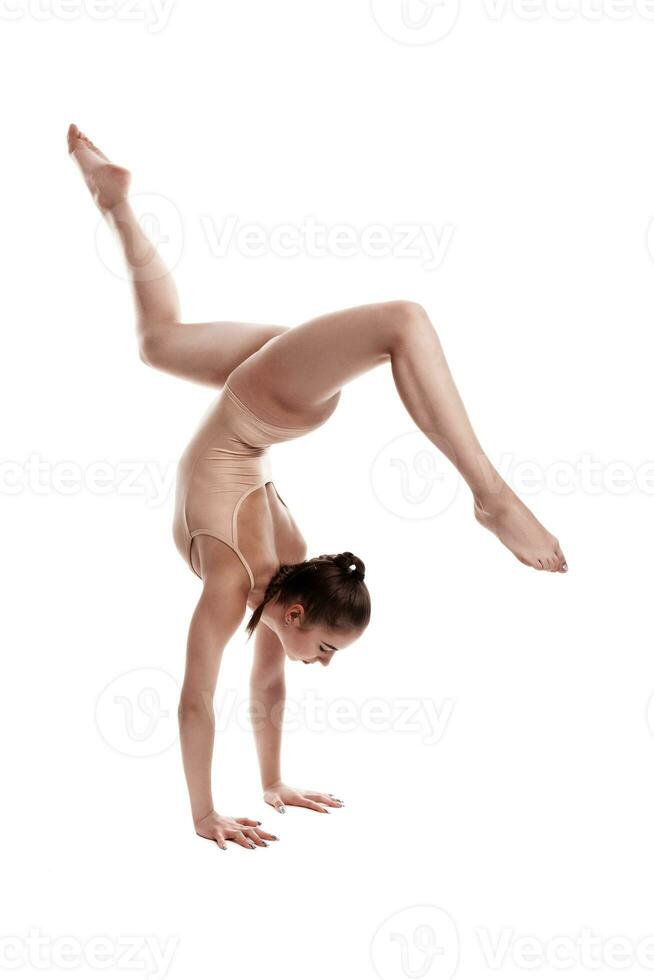 flexível menina ginasta dentro bege malha é realizando a exercício em pé em dela mãos enquanto posando isolado em branco fundo. fechar-se. foto