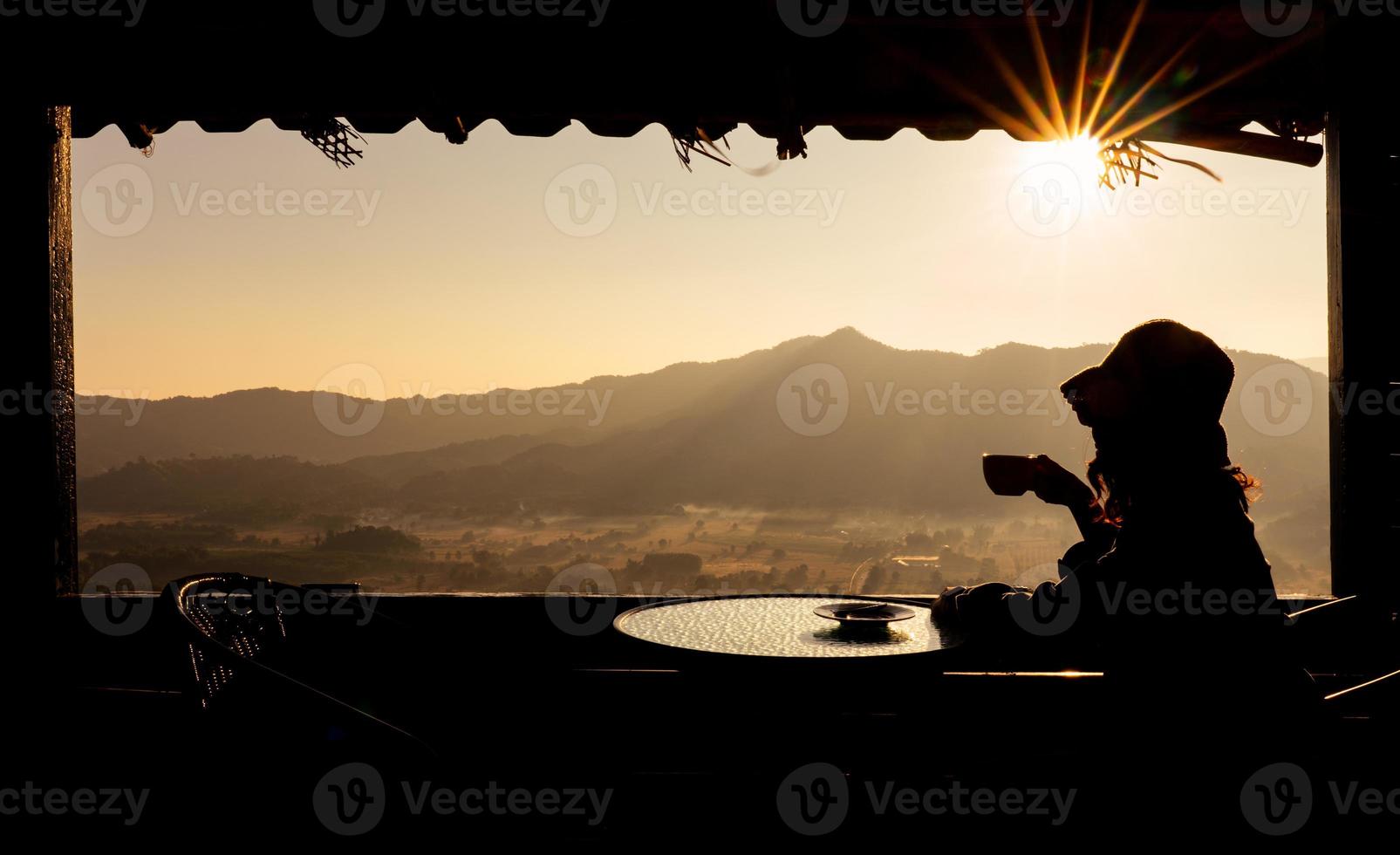 jovem mulher asiática sentada no quarto do hotel perto da janela, olhando a vista da montanha e beber café da manhã. turismo e conceito de férias foto