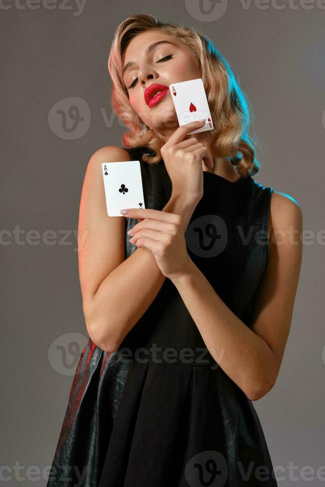 Loiras menina dentro Preto à moda vestir mostrando dois jogando cartões, posando contra cinzento fundo. jogos de azar entretenimento, pôquer, casino. fechar-se. foto