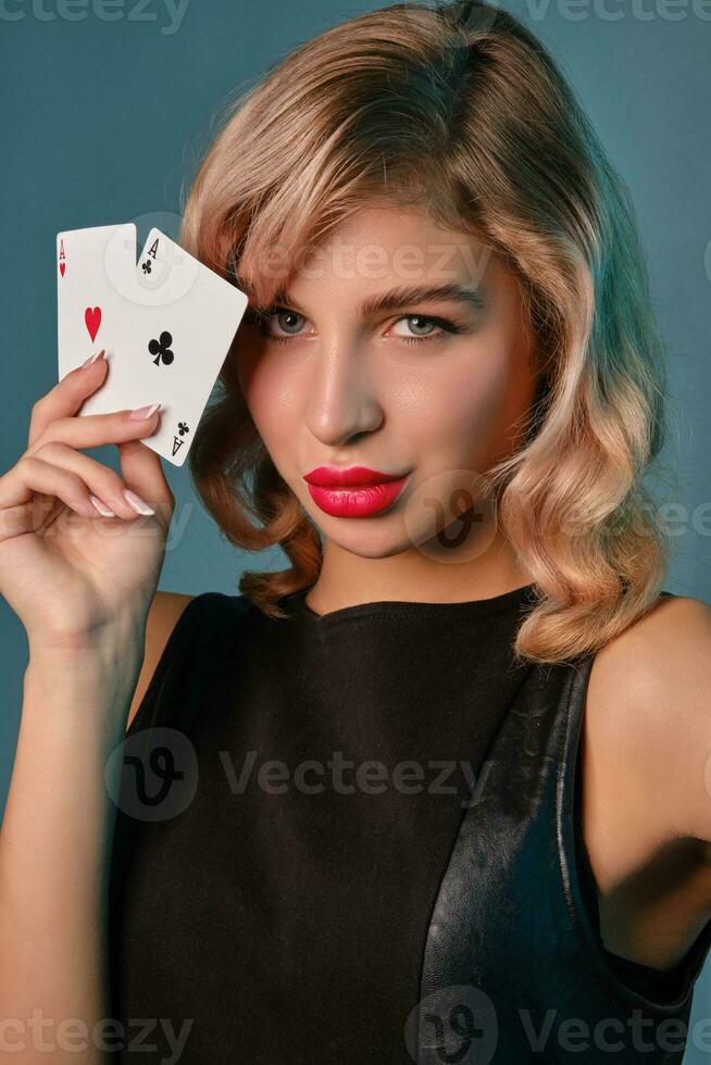 Loiras menina dentro Preto à moda vestir mostrando dois jogando cartões, posando contra azul fundo. jogos de azar entretenimento, pôquer, casino. fechar-se. foto