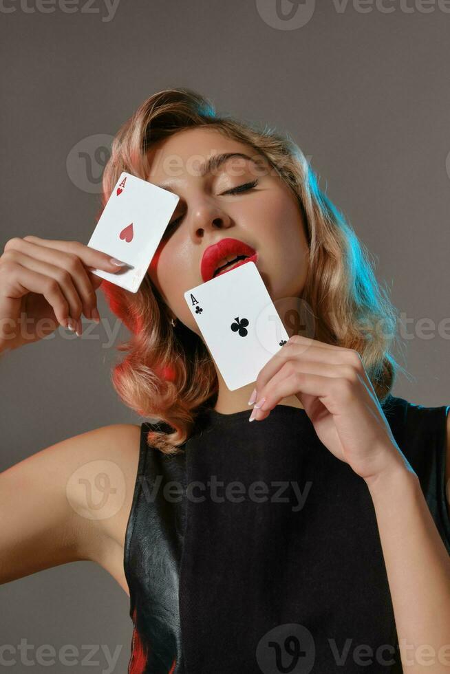Loiras menina dentro Preto à moda vestir mostrando dois jogando cartões, posando contra cinzento fundo. jogos de azar entretenimento, pôquer, casino. fechar-se. foto