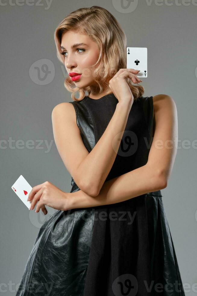 Loiras menina dentro Preto à moda vestir mostrando dois jogando cartões, posando contra cinzento fundo. jogos de azar entretenimento, pôquer, casino. fechar-se. foto