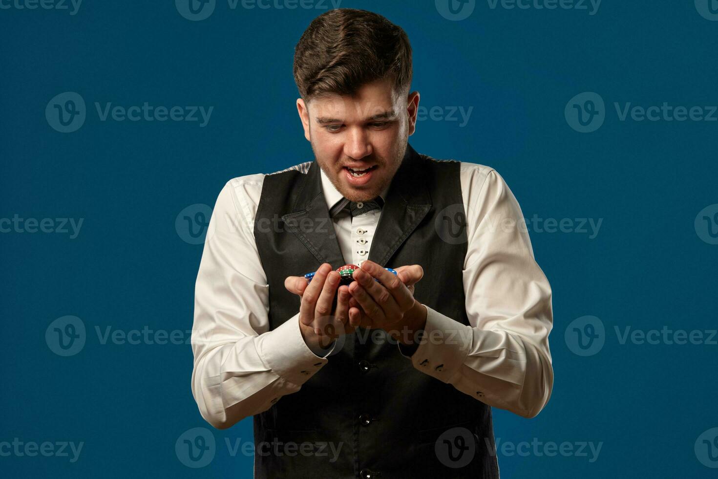 novato dentro pôquer, dentro Preto colete e branco camisa. segurando alguns colori salgadinhos. posando contra azul fundo. jogatina, casino. fechar-se. foto