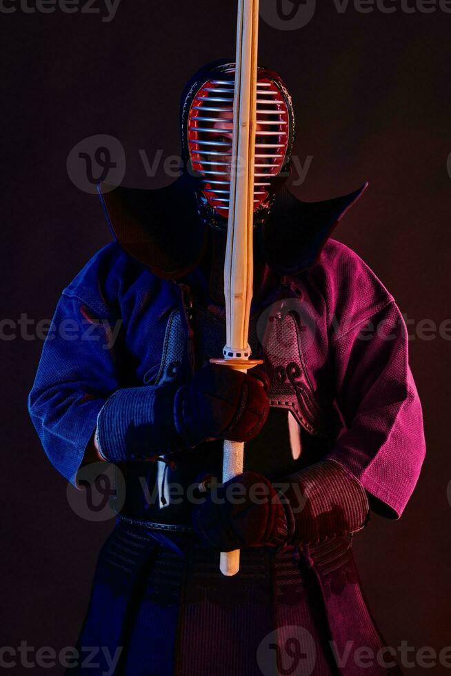 fechar acima tomada, kendo lutador vestindo dentro a armaduras, tradicional quimono, capacete praticando marcial arte com Shinai bambu espada, Preto fundo. foto