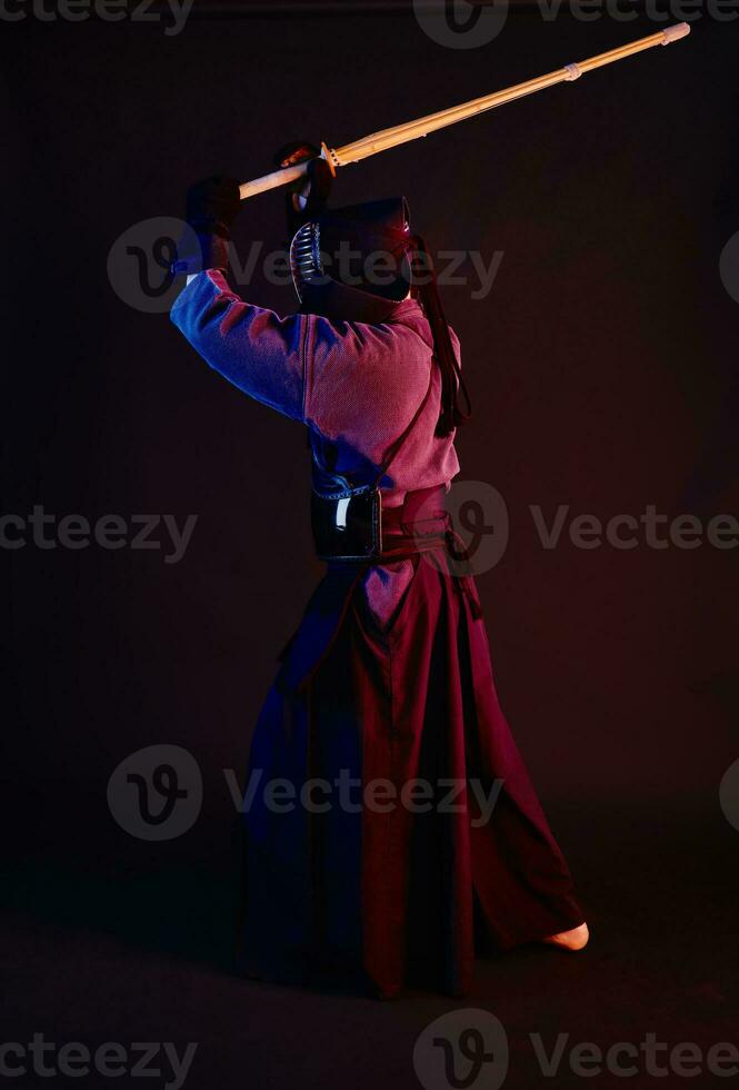 fechar acima tomada, kendo lutador vestindo dentro a armaduras, tradicional quimono, capacete praticando marcial arte com Shinai bambu espada, Preto fundo. foto