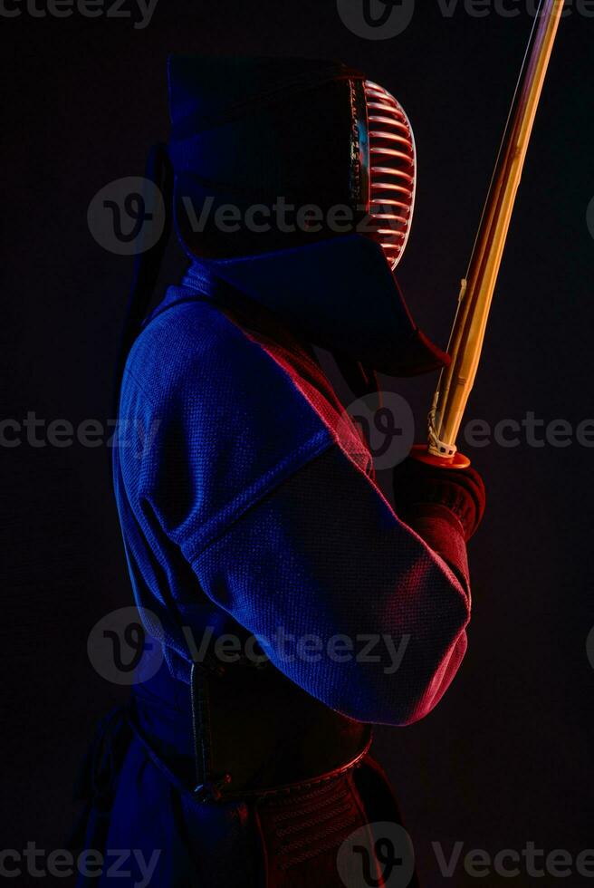 fechar acima tomada, kendo lutador vestindo dentro a armaduras, tradicional quimono, capacete praticando marcial arte com Shinai bambu espada, Preto fundo. foto