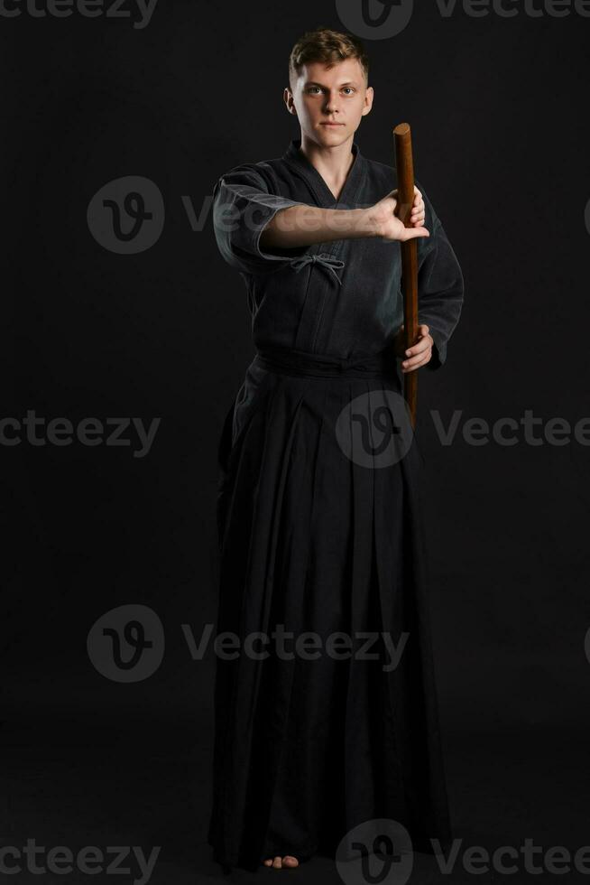 kendo guru vestindo dentro uma tradicional japonês quimono é praticando marcial arte com a Shinai bambu espada contra uma Preto estúdio fundo. foto