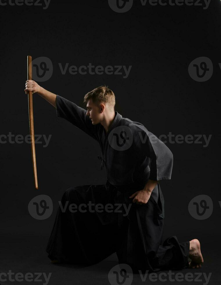 kendo guru vestindo dentro uma tradicional japonês quimono é praticando marcial arte com a Shinai bambu espada contra uma Preto estúdio fundo. foto