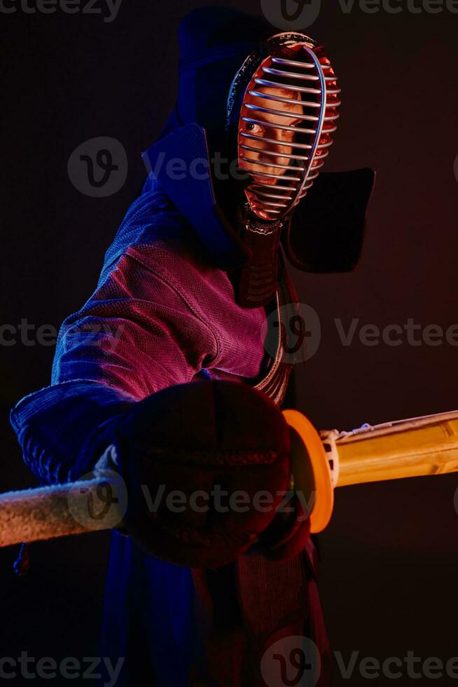 fechar acima tomada, kendo lutador vestindo dentro a armaduras, tradicional quimono, capacete praticando marcial arte com Shinai bambu espada, Preto fundo. foto