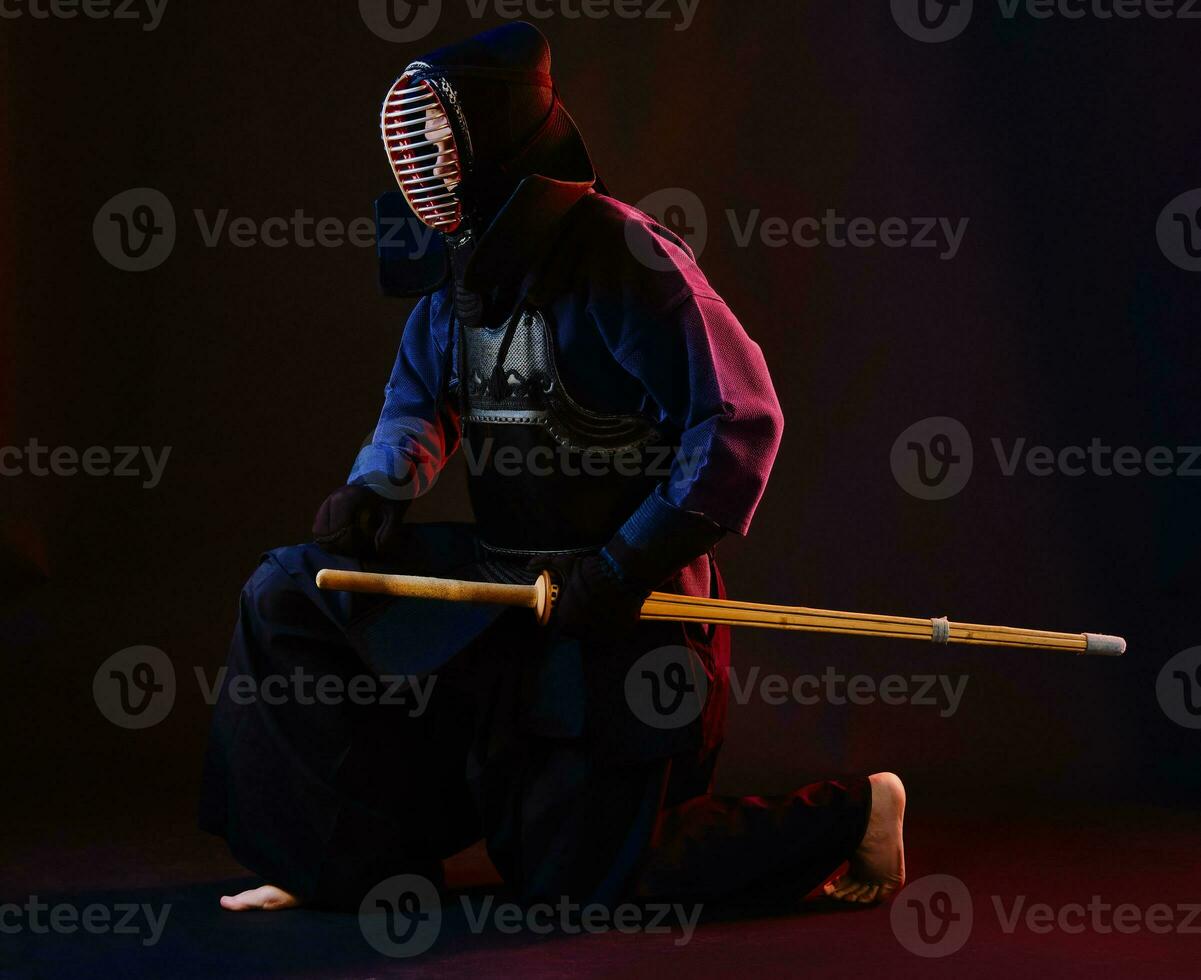 fechar acima tomada, kendo lutador vestindo dentro a armaduras, tradicional quimono, capacete praticando marcial arte com Shinai bambu espada, Preto fundo. foto