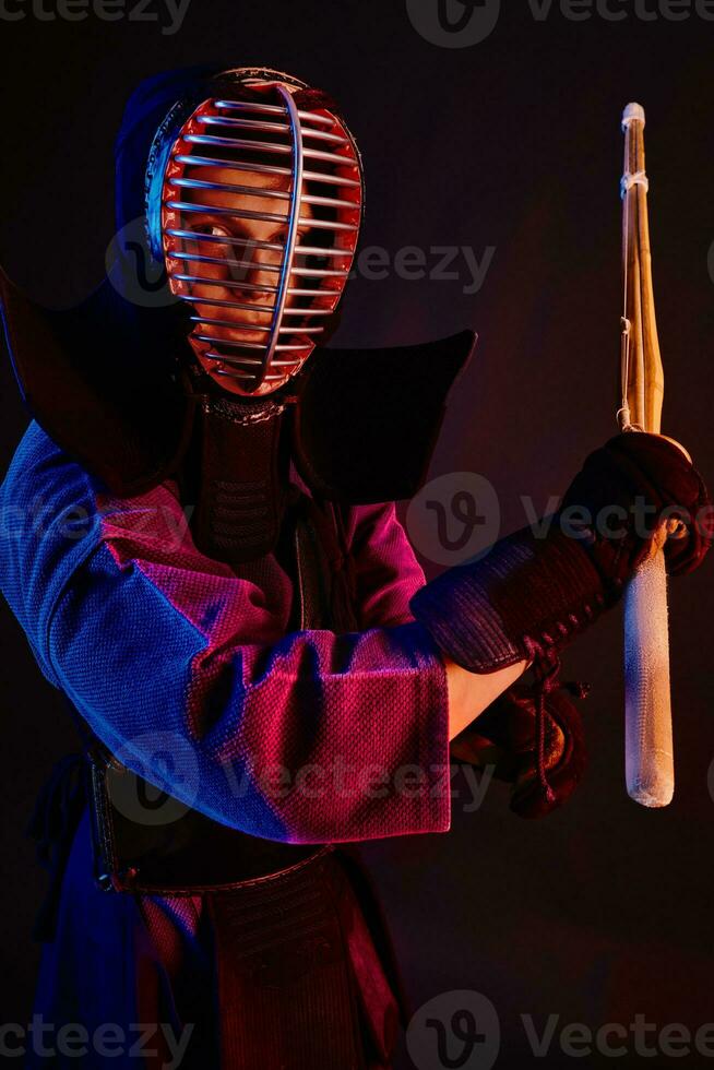 fechar acima tomada, kendo lutador vestindo dentro a armaduras, tradicional quimono, capacete praticando marcial arte com Shinai bambu espada, Preto fundo. foto