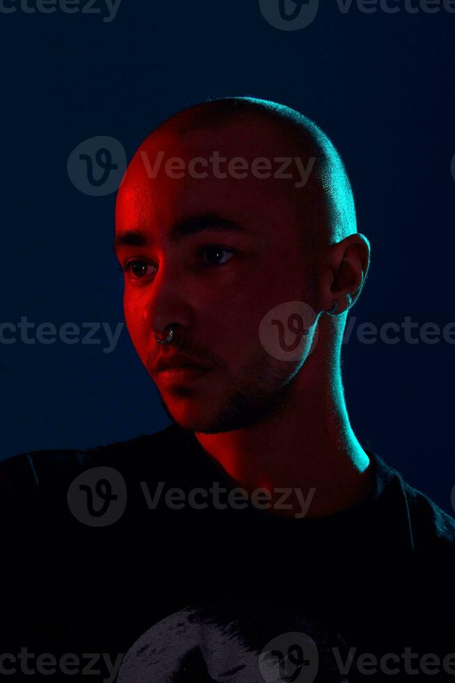 estúdio tiro do uma jovem tatuado Careca homem posando contra uma azul fundo. anos 90 estilo. foto