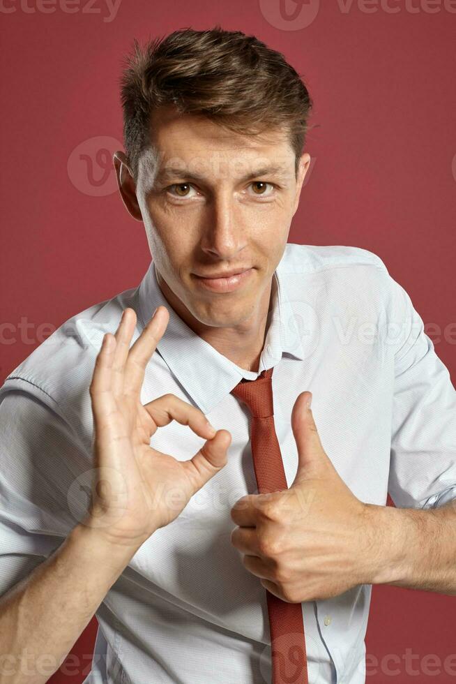 retrato do uma jovem moreno homem posando dentro uma estúdio contra uma vermelho fundo. foto