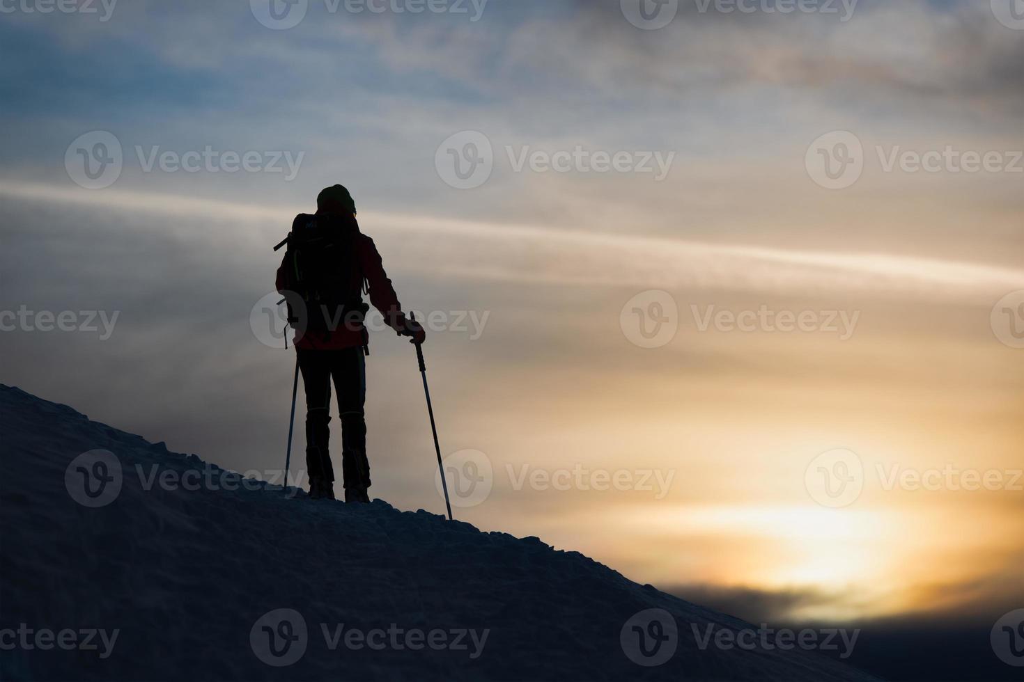 um esquiador alpinista vê o sol se pôr foto