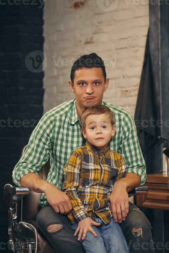 jovem bonito pai e dele pequeno à moda filho às barbearia esperando para barbeiro foto