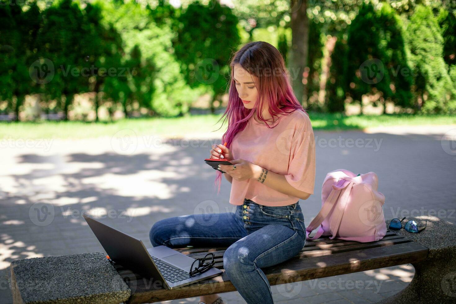 mulher escrevendo dentro uma caderno sentado em uma de madeira Banco dentro a parque. menina trabalhando ao ar livre em portátil computador, cópia de espaço. foto