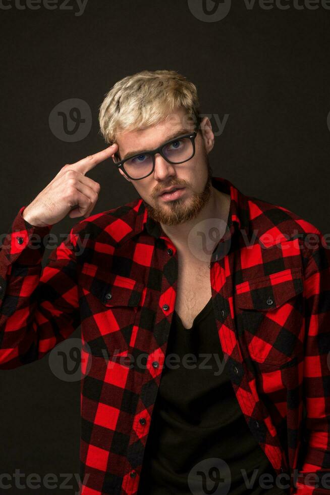 bonito na moda jovem cara às a estúdio em Preto fundo. ele desgasta barba e uma xadrez camisa foto