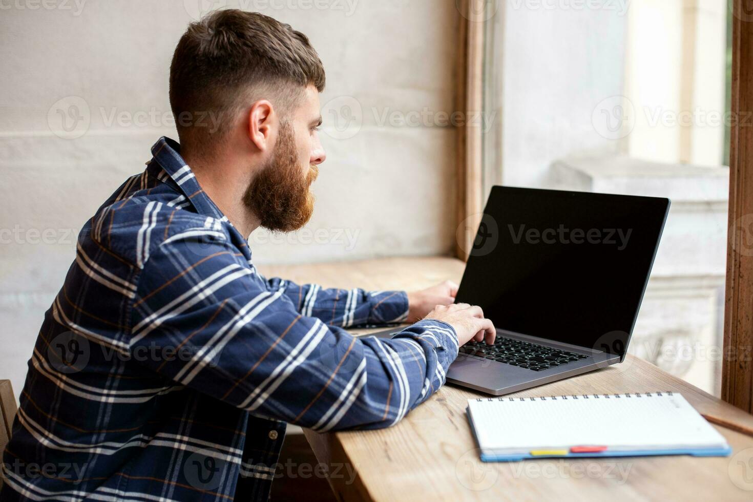 jovem homem conversando através da netbook durante trabalhos pausa dentro café comprar, masculino sentado dentro frente aberto computador portátil computador com em branco cópia de espaço tela. foto