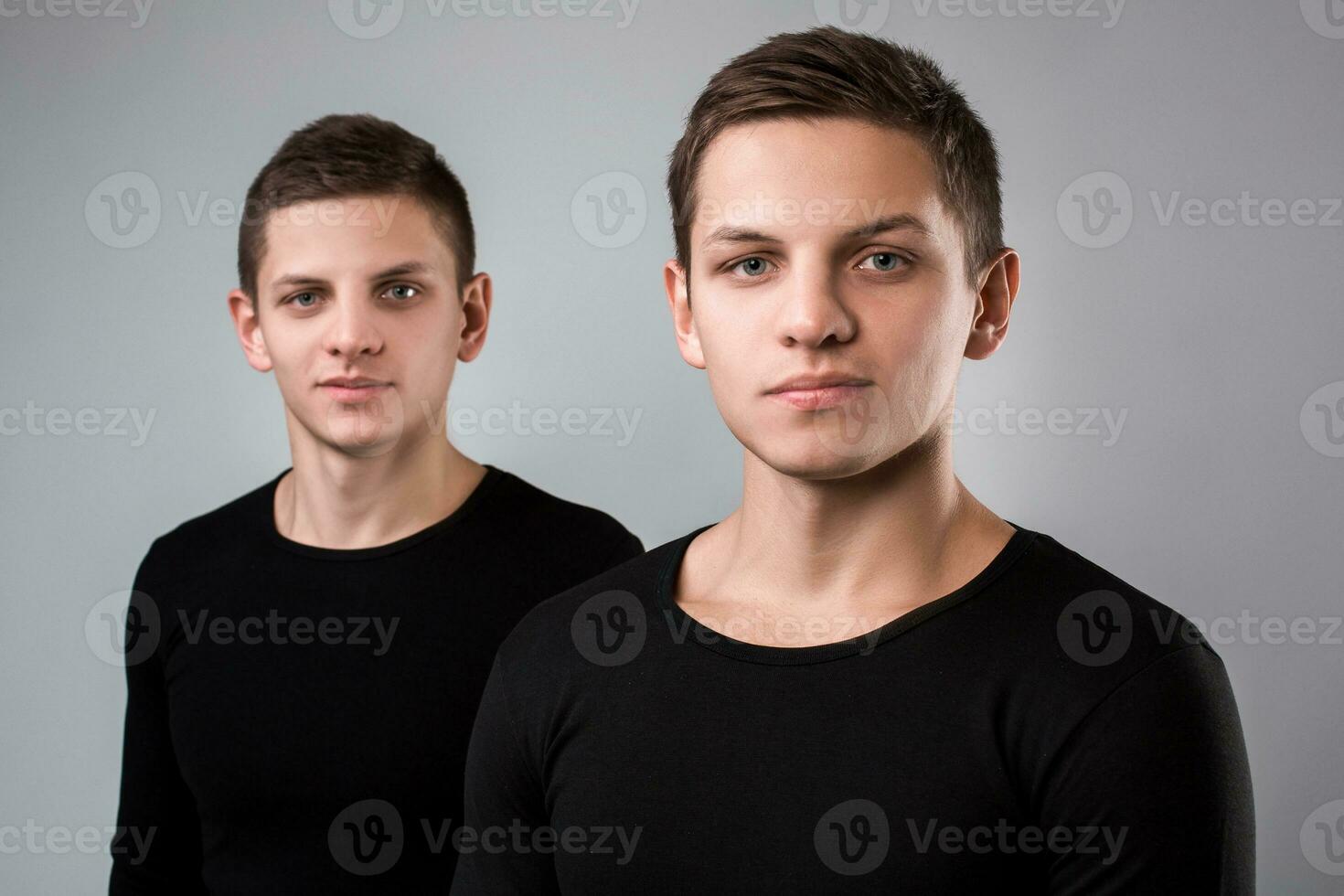 a dois gêmeo irmão ficar de pé em a cinzento fundo foto