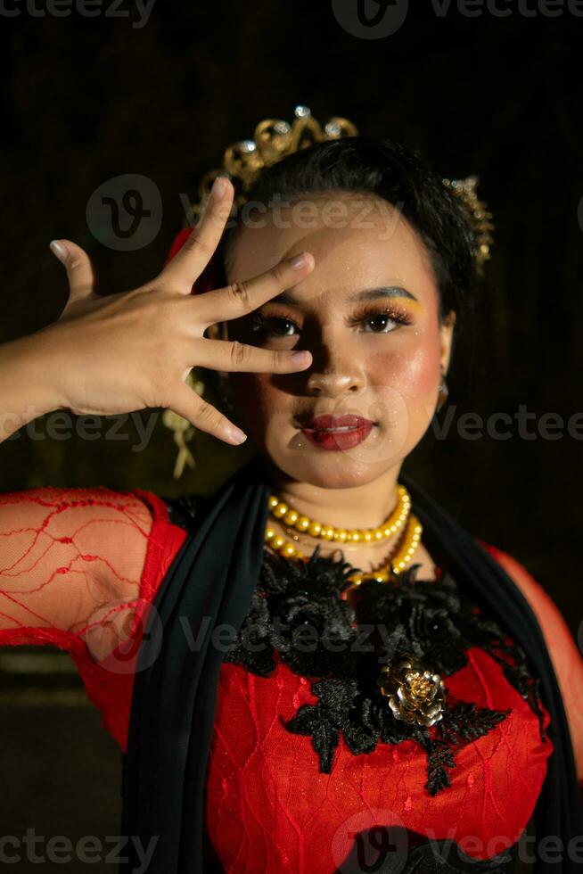 a indonésio dançarino dentro vermelho roupas e uma Preto cachecol poses com muito encaracolado e lindo dedos foto