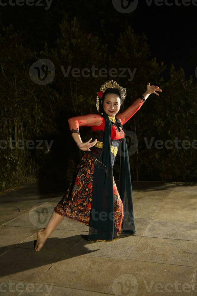 uma javanese dançarino vestindo uma Preto xaile e jasmim em dela cabeça enquanto dançando em etapa às noite foto