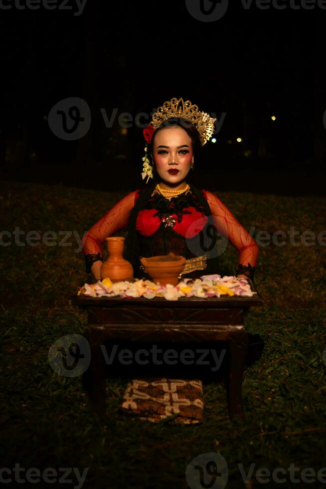 Largo tiro do a ásia menina dentro tradicional roupas sentado dentro uma floresta com uma mesa cheio do flores foto