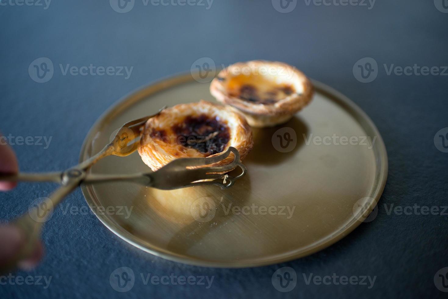 close up de uma mão com pinças de servir para escolher um delicioso bolo de belém, pasteis de belem, seguindo a receita tradicional portuguesa. gastronomia. foto