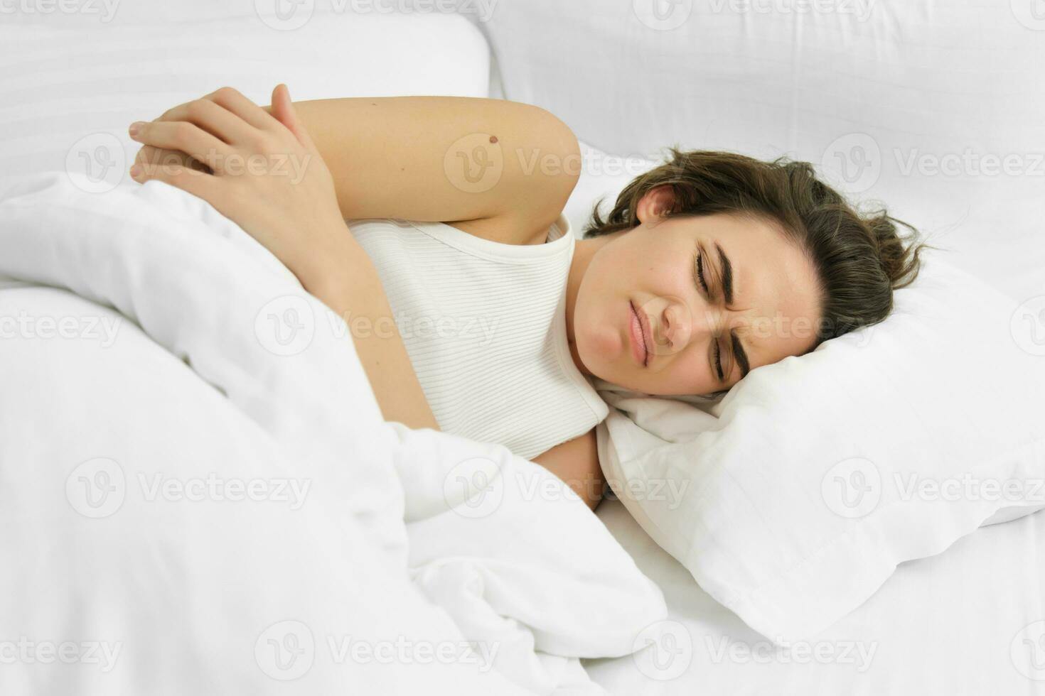 jovem mulher deitado dentro cama com estômago dor, tem doloroso cólicas, menstrual dor foto