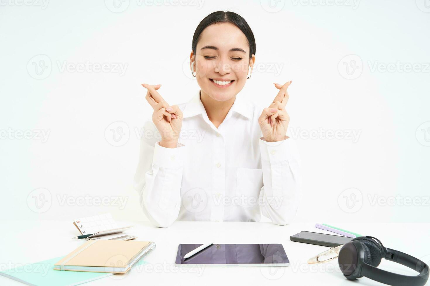 esperançoso ásia empresária, Cruz dedos para Boa sorte, senta dentro local de trabalho escritório e faz desejar, branco fundo foto