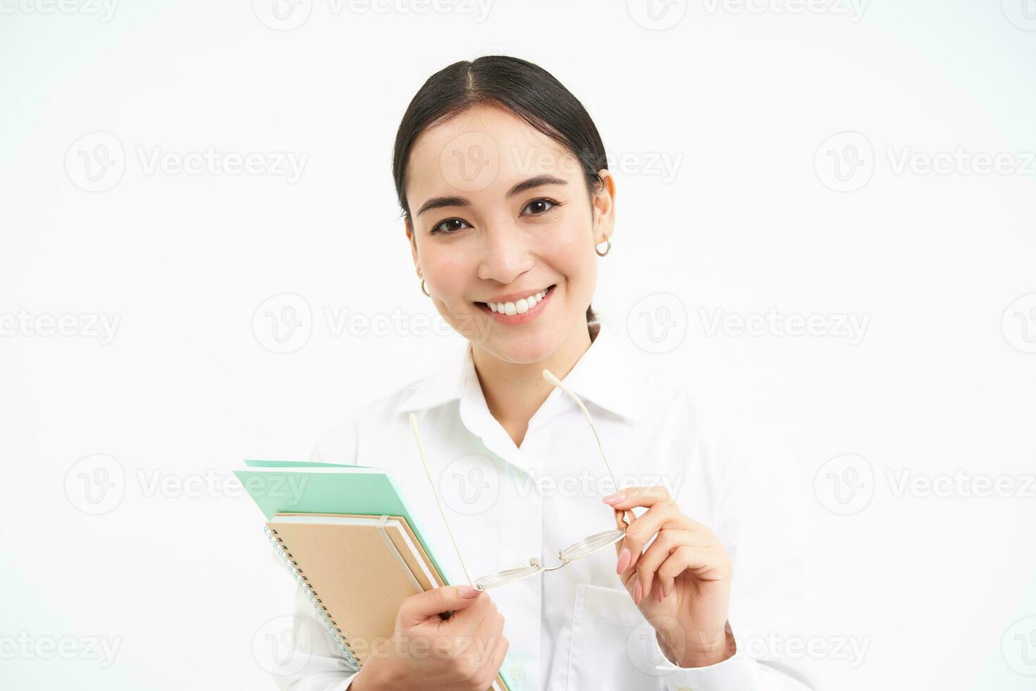 bem sucedido jovem ásia mulher, professor com cadernos, olhando confiante e sorridente, branco estúdio fundo foto