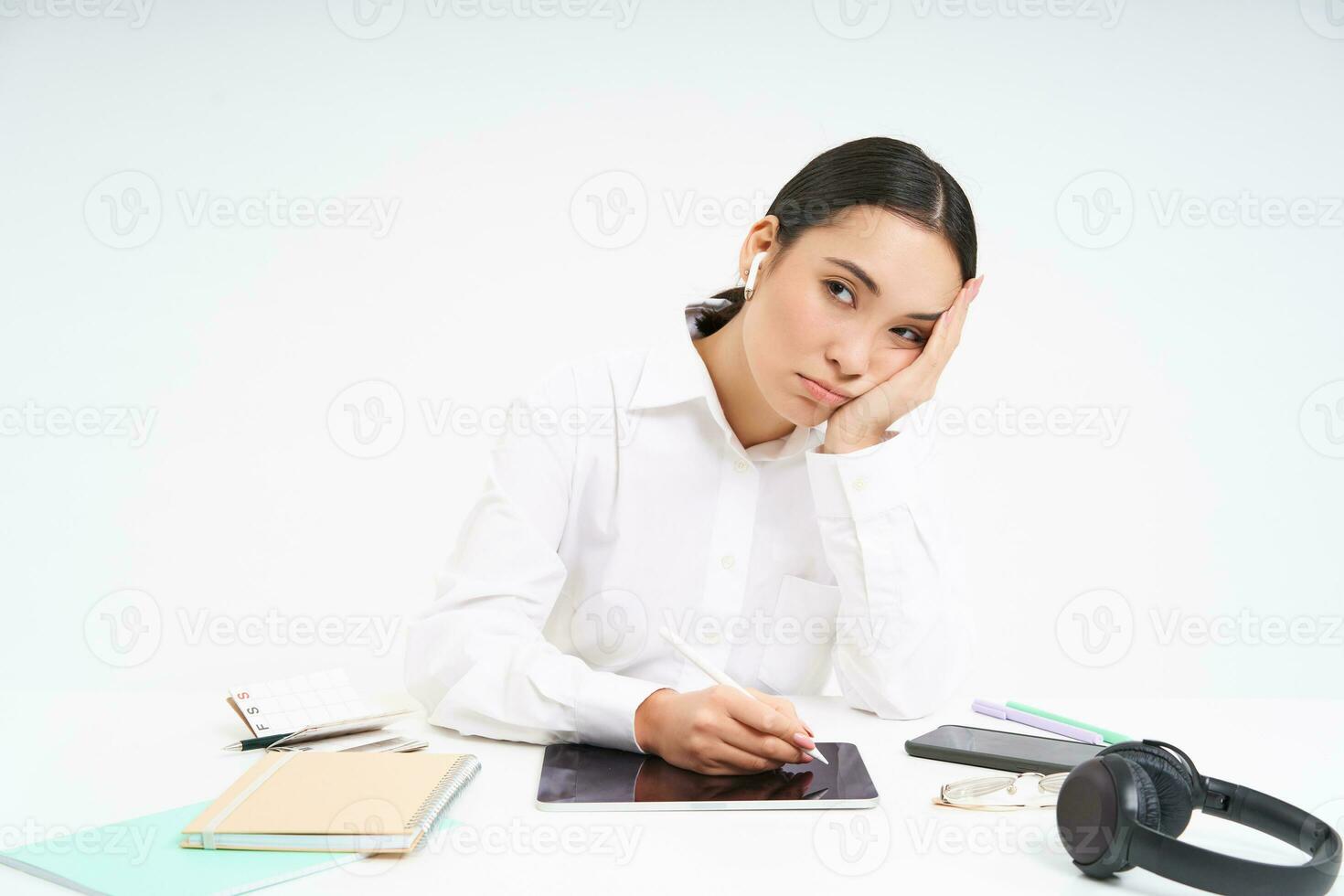 cansado e entediado coreano mulher dentro escritório, empregado senta com digital tábua, escuta música dentro fones de ouvido e parece cansado, branco fundo foto