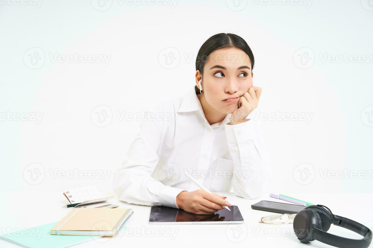 cansado e entediado coreano mulher dentro escritório, empregado senta com digital tábua, escuta música dentro fones de ouvido e parece cansado, branco fundo foto