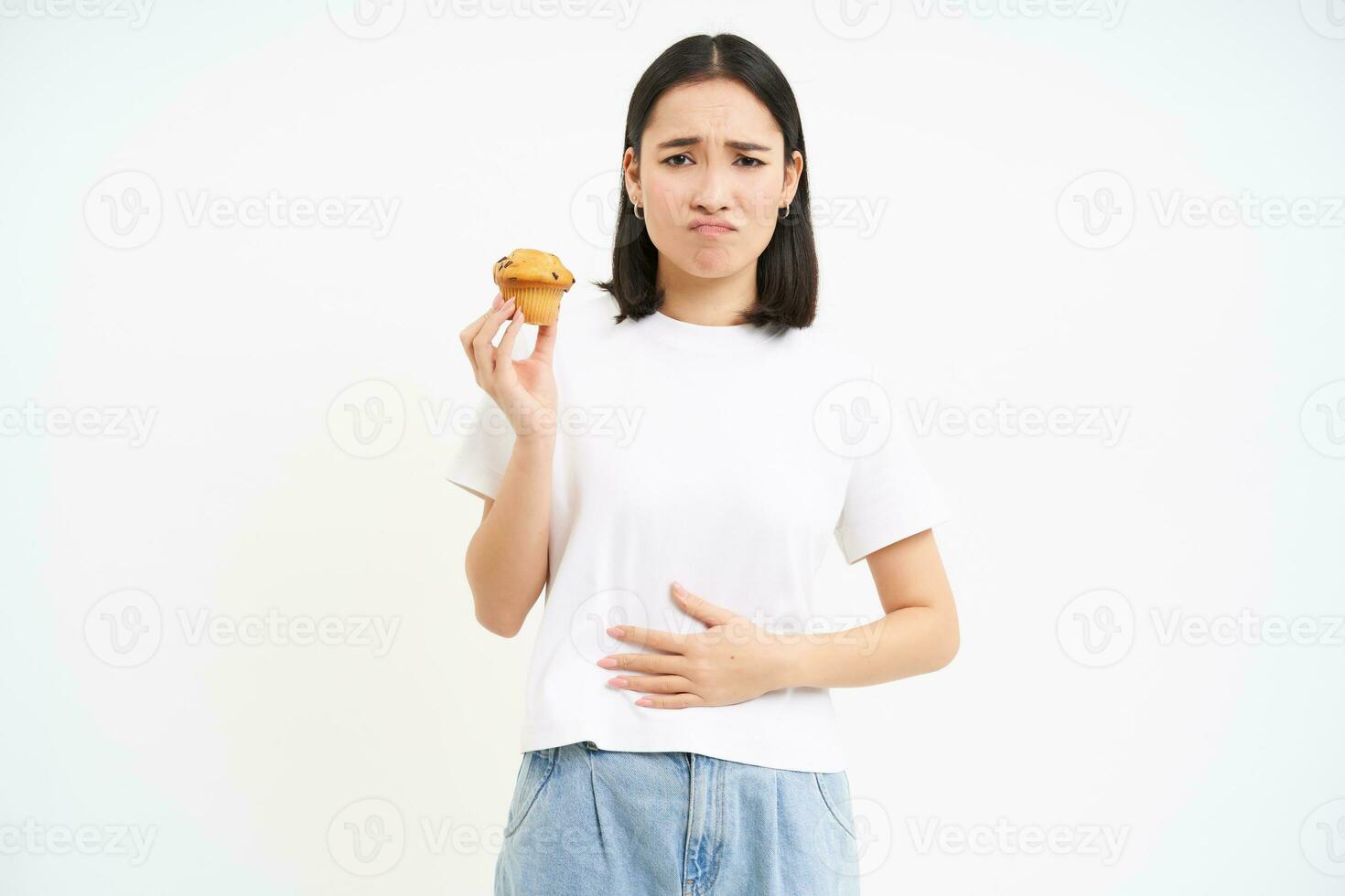 retrato do ásia mulher sentindo-me dor dentro estômago, desconforto depois de comida, segurando Bolinho e olhando infeliz, branco fundo foto