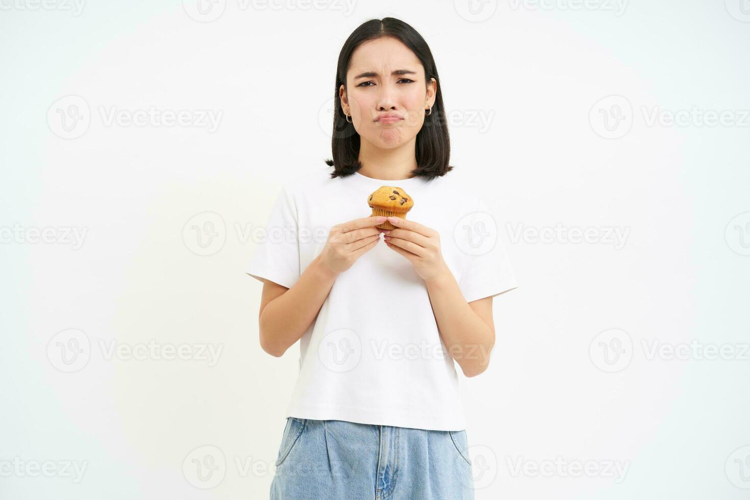 retrato do miserável menina com Bolinho, triste sem doces, hipócrita comer pastelaria, ser em dieta, branco fundo foto