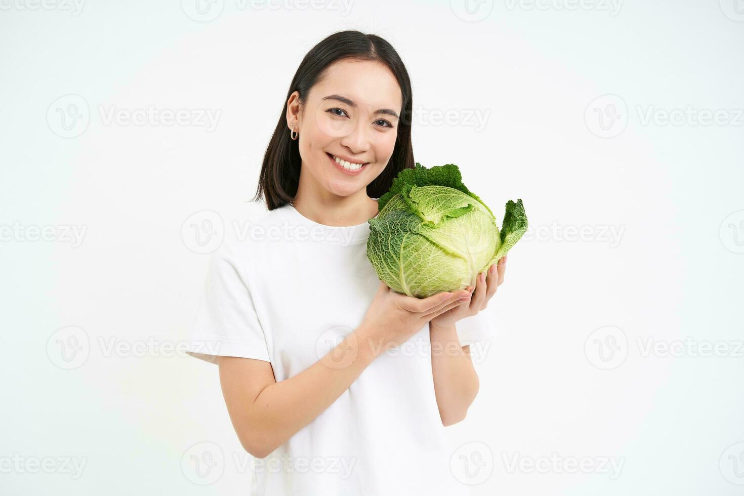 lindo e saudável jovem mulher sorridente, mostrando verde repolho, orgânico alface, branco estúdio fundo foto