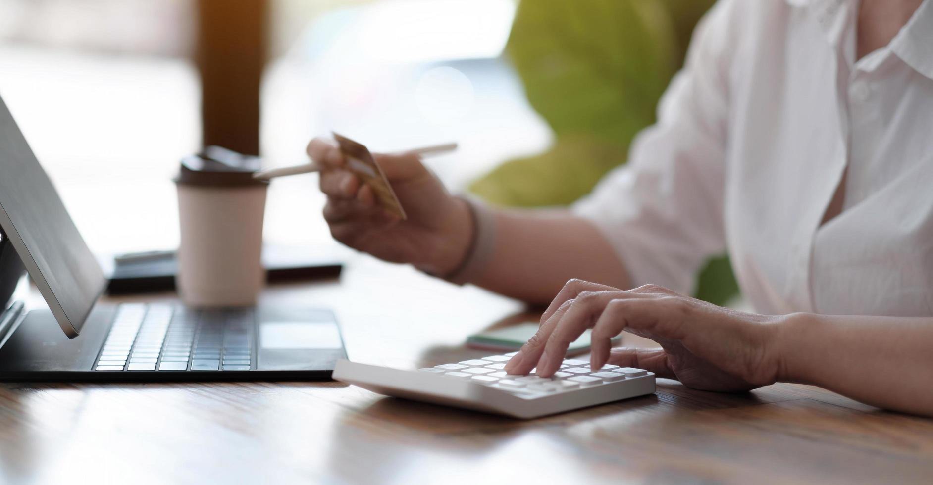 contador de mulher trabalhando no escritório usando a calculadora e segurando o cartão de crédito, closeup de mãos, banner panorâmico. conceito de compras online. foto