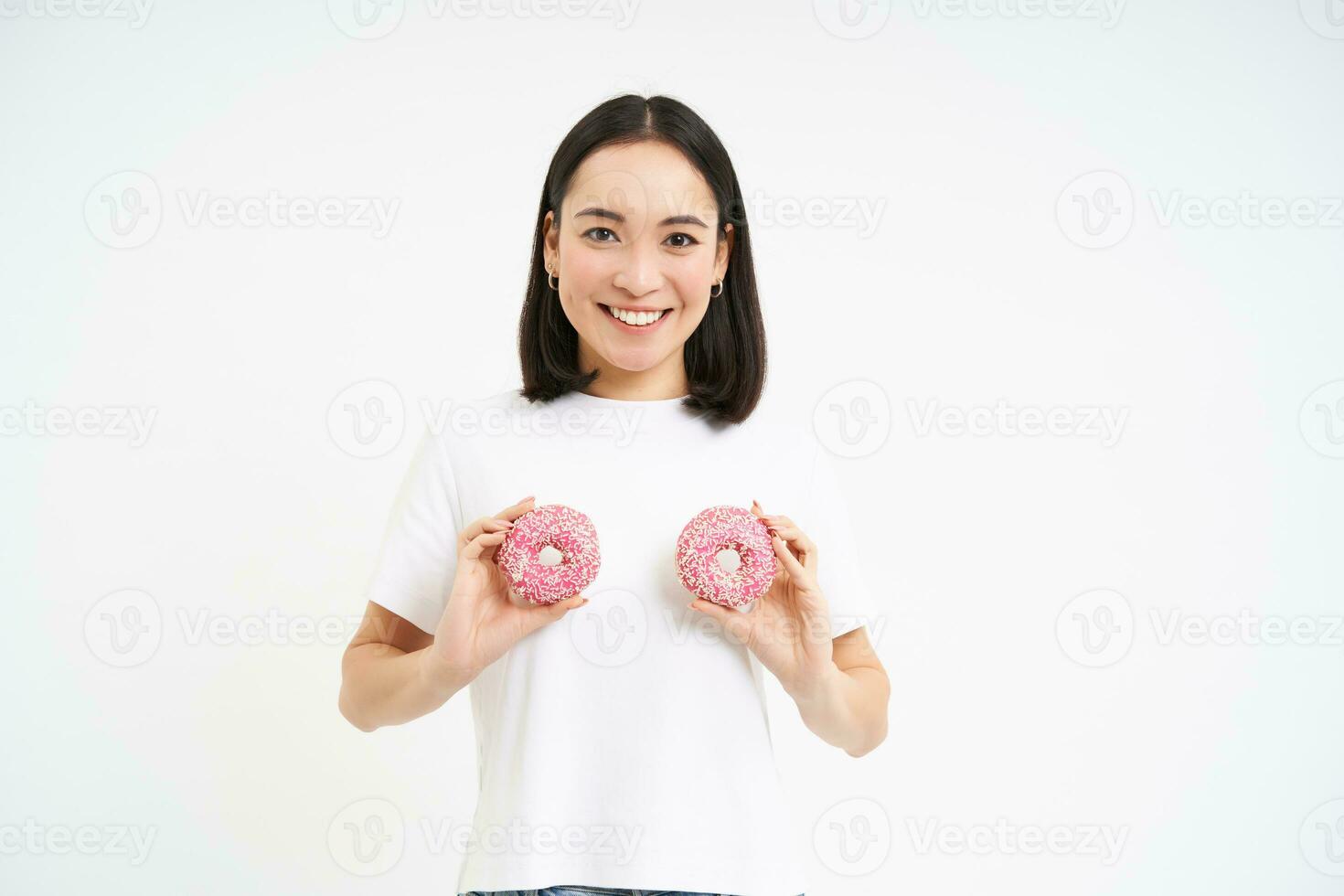 fofa sorridente mulher detém dois donuts perto dela peito e olhando feliz, comendo sobremesa, branco estúdio fundo foto